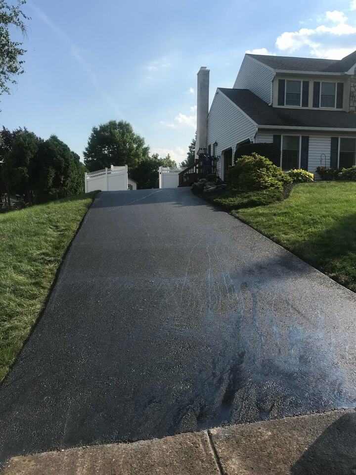 Freshly paved asphalt driveway leading up to a two-story home