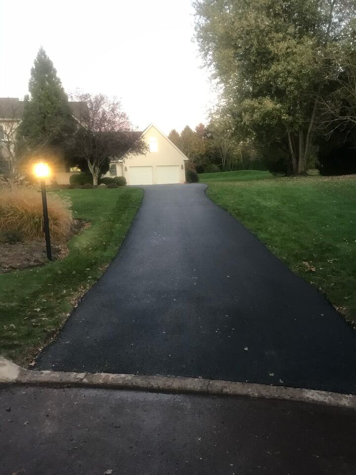 Newly paved asphalt driveway curving up to a house, with a lamppost at the edge