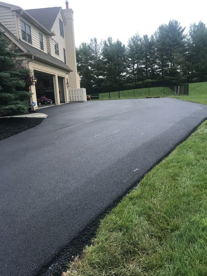 Wide new asphalt driveway beside a home's attached garage