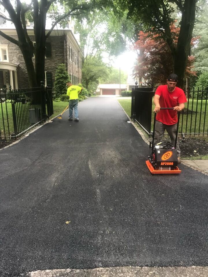 DeRosato crew member compacting fresh asphalt on a gated driveway