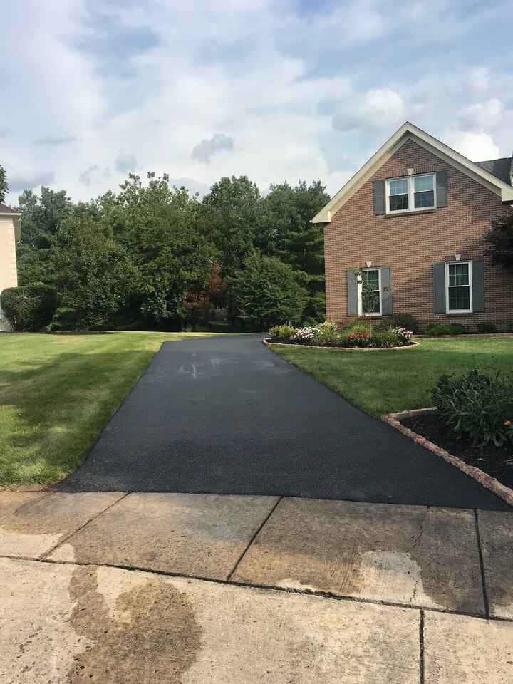 New asphalt driveway leading to a brick home with landscaped beds