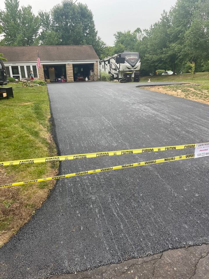 Wide freshly paved driveway taped off while it cures, in front of a ranch home
