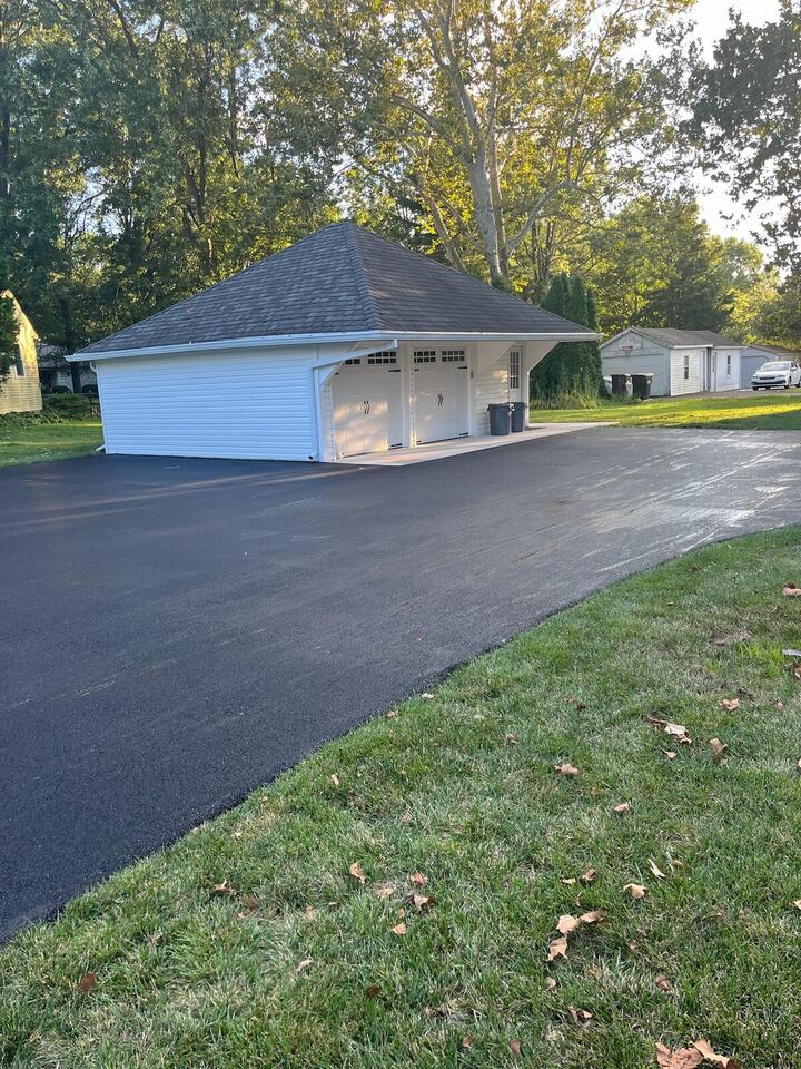 New asphalt driveway and parking area in front of a detached white garage