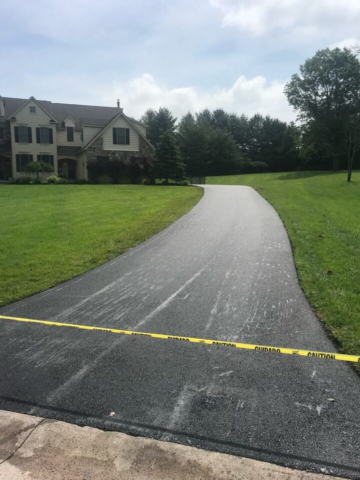 Long new asphalt driveway leading to a stone-front home, taped off at the street